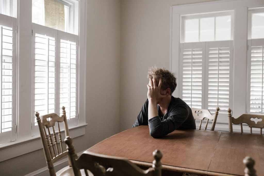 Person sitting at kitchen table with leaning on hand looking out window